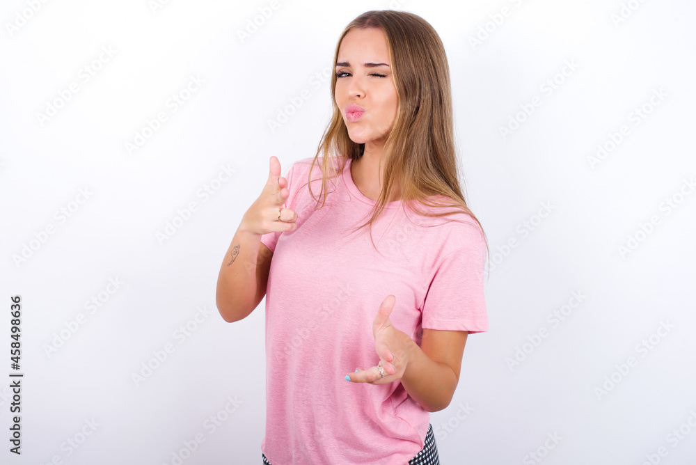 Hey you, bang. Joyful and charismatic good-looking beautiful blonde girl wearing pink t-shirt on white background winking and pointing with finger pistols at camera happily and cheeky. Hey you, bang. Joyful and charismatic good-looking beautiful blonde girl wearing pink t-shirt on white background winking and pointing with finger pistols at camera happily and cheeky.
