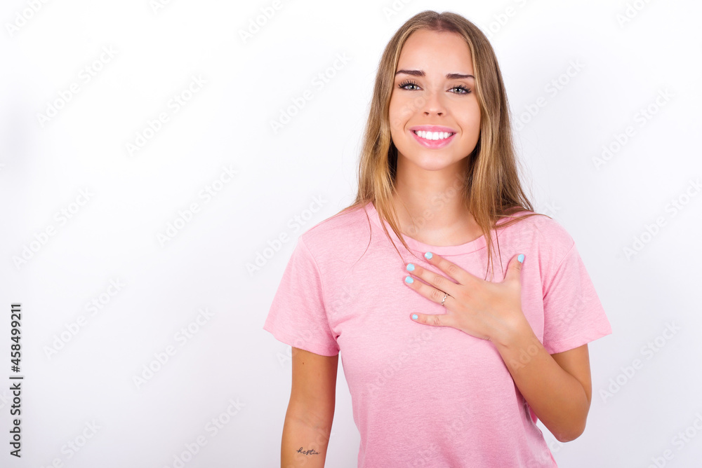 beautiful blonde girl wearing pink t-shirt on white background smiles toothily cannot believe eyes expresses good emotions and surprisement beautiful blonde girl wearing pink t-shirt on white background smiles toothily cannot believe eyes expresses good emotions and surprisement