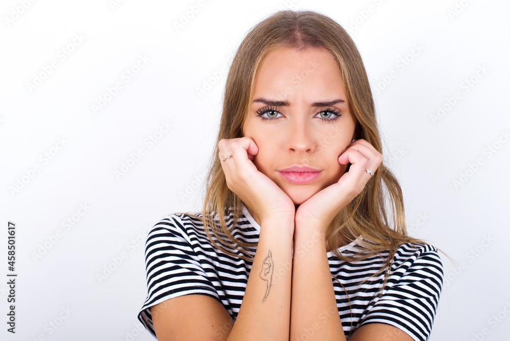 Portrait of sad beautiful blonde girl wearing striped t-shirt on white background hands face Portrait of sad beautiful blonde girl wearing striped t-shirt on white background hands face