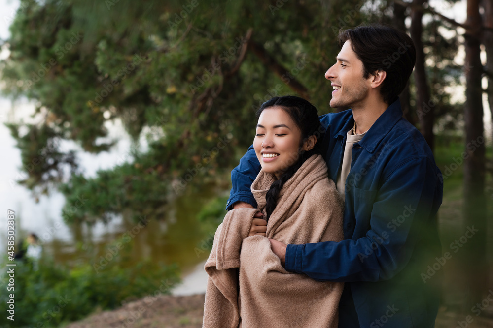 Smiling man hugging asian girlfriend in blanket outdoors Smiling man hugging asian girlfriend in blanket outdoors