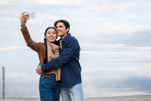 Asian woman taking selfie with boyfriend on beach