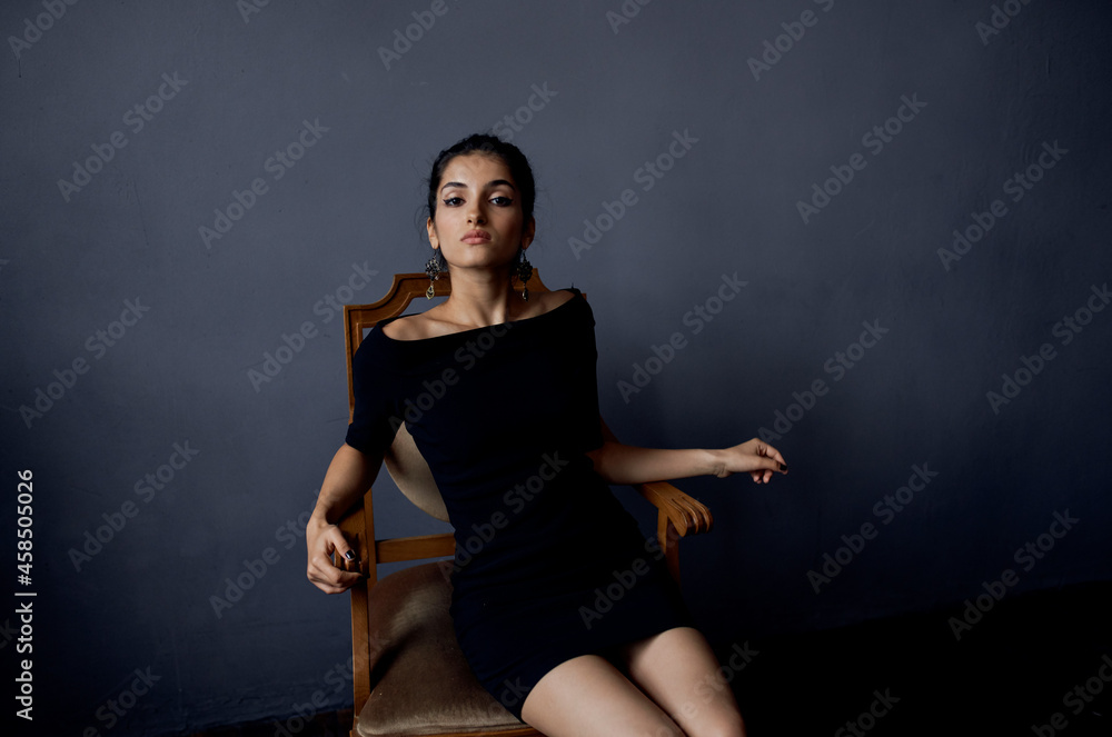 pretty woman earrings jewelry posing near the chair black dress dark background pretty woman earrings jewelry posing near the chair black dress dark background
