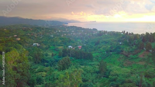 The movement of the drone along the coast of the sea and the green forest, a village or village with dense green vegetation is located near the coastal territory. Georgia. The Black Sea. photo