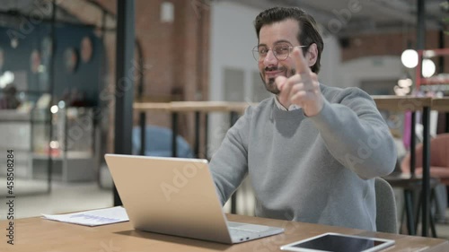 Young Man Pointing at Camera while using Laptop in Office