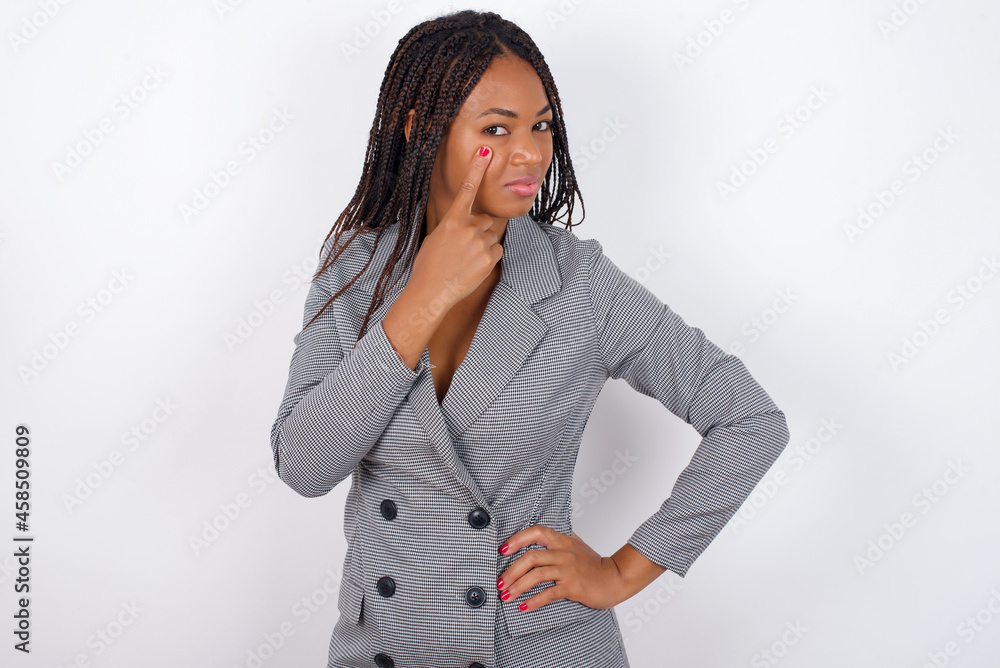 Young African American businesswoman with braids on white wall, looking, observing, keeping an eye on an object in front, or watching out for something. Young African American businesswoman with braids on white wall, looking, observing, keeping an eye on an object in front, or watching out for something.