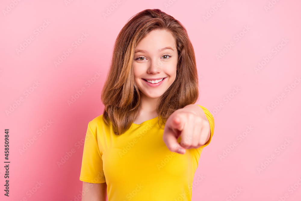 Photo of funny blond teenager girl point camera wear yellow t-shirt isolated on pink color background Photo of funny blond teenager girl point camera wear yellow t-shirt isolated on pink color background