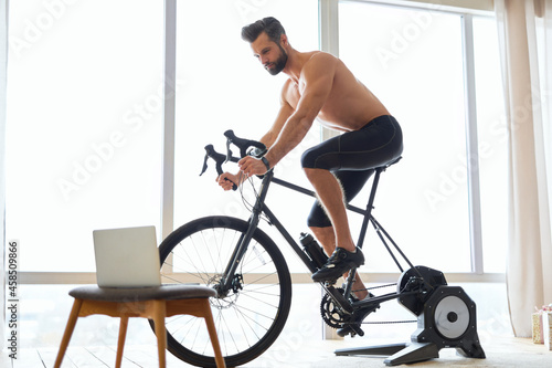 Athletic young man using bicycle trainer at home