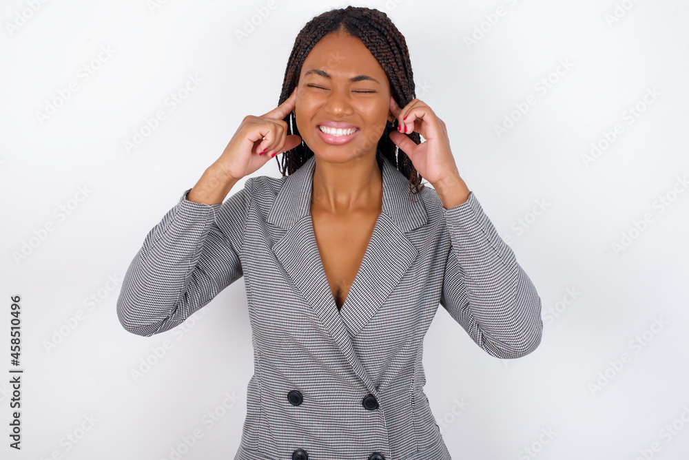 Stop making this annoying sound! Unhappy stressed out Young African American businesswoman with braids on white wall making worry face, plugging ears with fingers, irritated with loud noise. Stop making this annoying sound! Unhappy stressed out Young African American businesswoman with braids on white wall making worry face, plugging ears with fingers, irritated with loud noise.