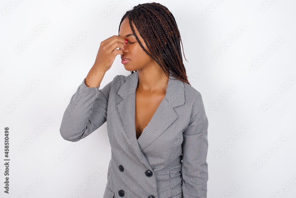 Very upset, Young African American businesswoman with braids on white wall touching nose between closed eyes, wants to cry, having stressful relationship or having troubles with work Very upset, Young African American businesswoman with braids on white wall touching nose between closed eyes, wants to cry, having stressful relationship or having troubles with work