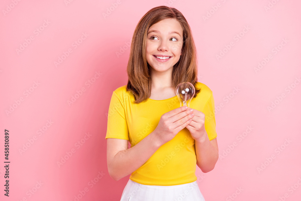Photo of young girl happy positive smile hold light bulb think look empty space idea isolated over pink color background Photo of young girl happy positive smile hold light bulb think look empty space idea isolated over pink color background