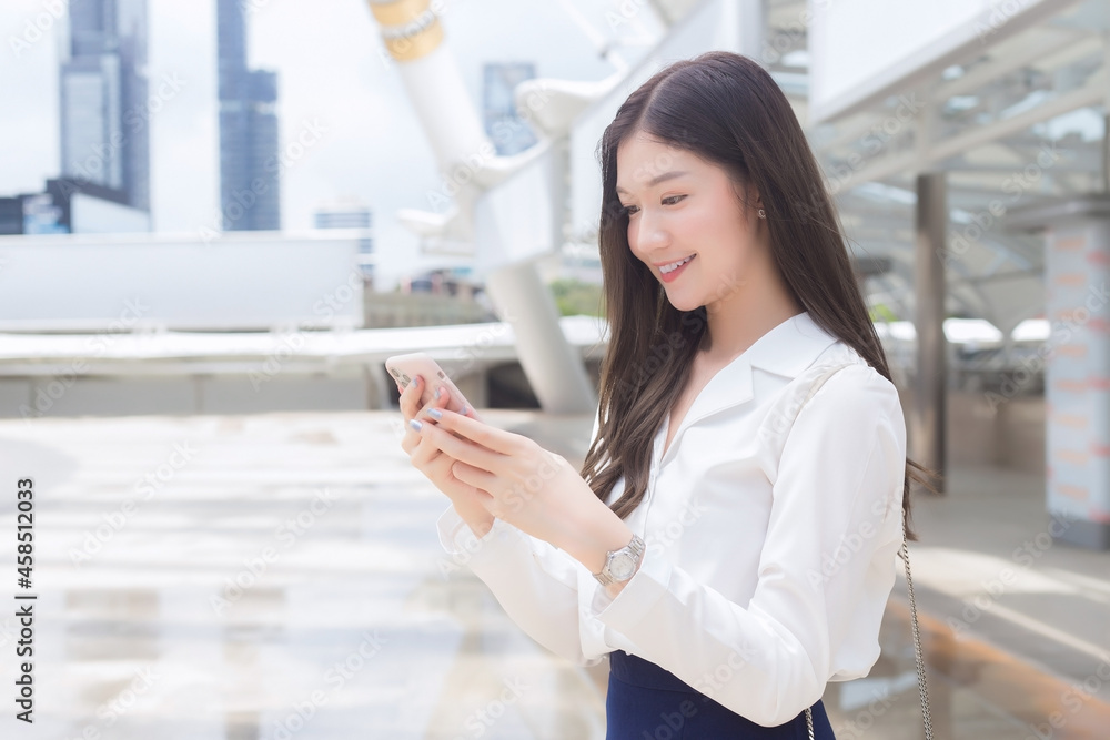 Young Asian Business woman is going to the office or workplace which she holds smartphone in her hands in business background theme.