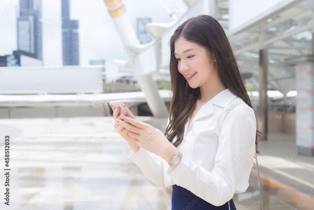 Young Asian Business woman is going to the office or workplace which she holds smartphone in her hands in business background theme. Young Asian Business woman is going to the office or workplace which she holds smartphone in her hands in business background theme.