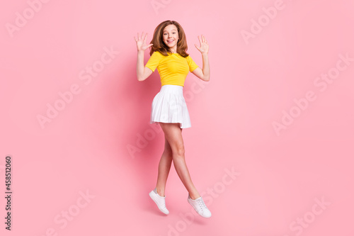 Full body profile side photo of young excited girl happy positive smile jump up hands wave hello isolated over pink color background