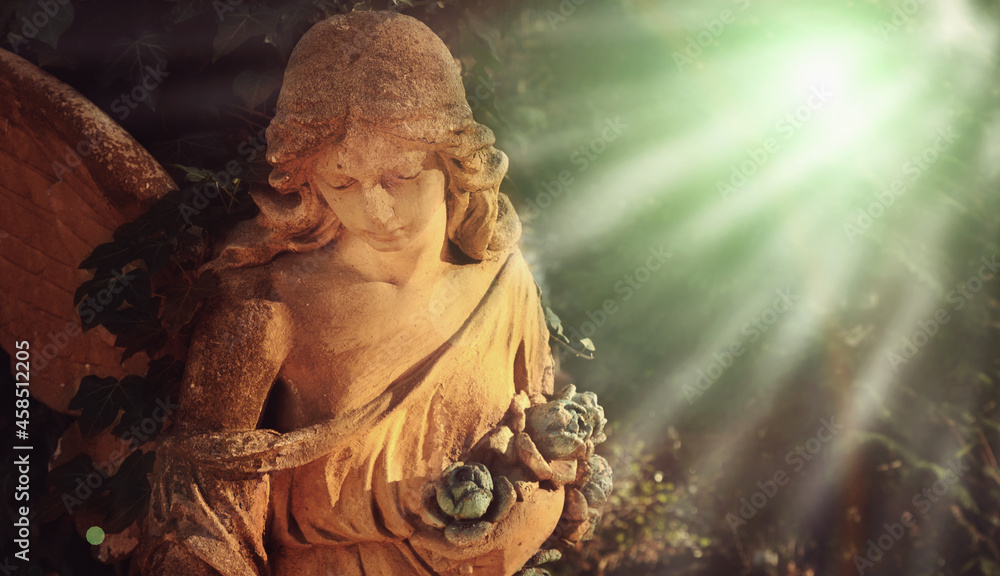 Guardian angel with wings in the sunlight. Antique statue.