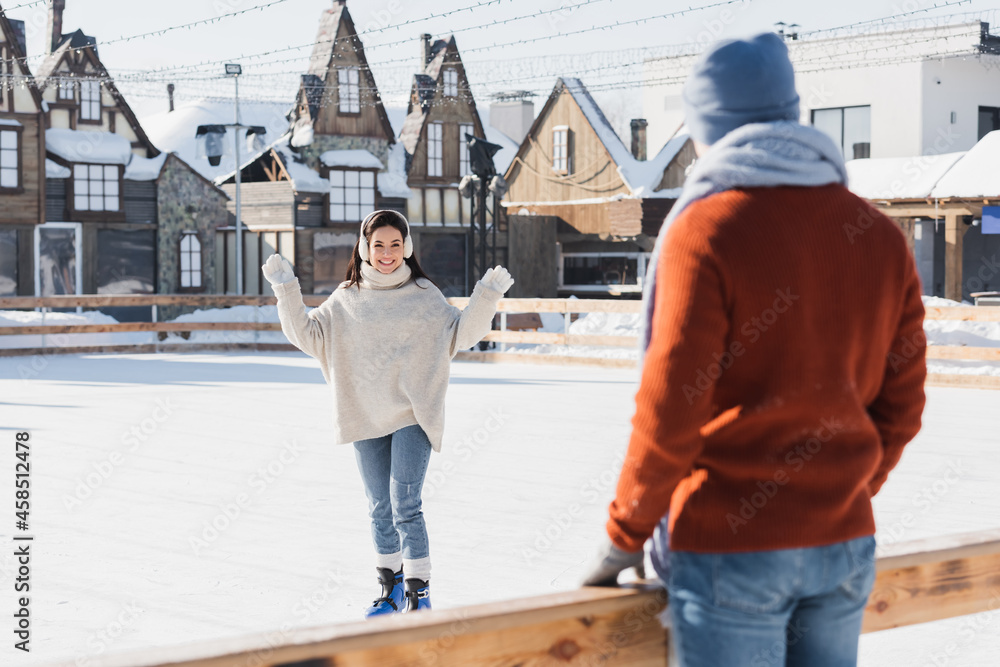 happy young woman in ice skates looking at blurred boyfriend on foreground
