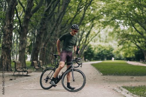 Cyclist in helmet and glasses drinking water at park