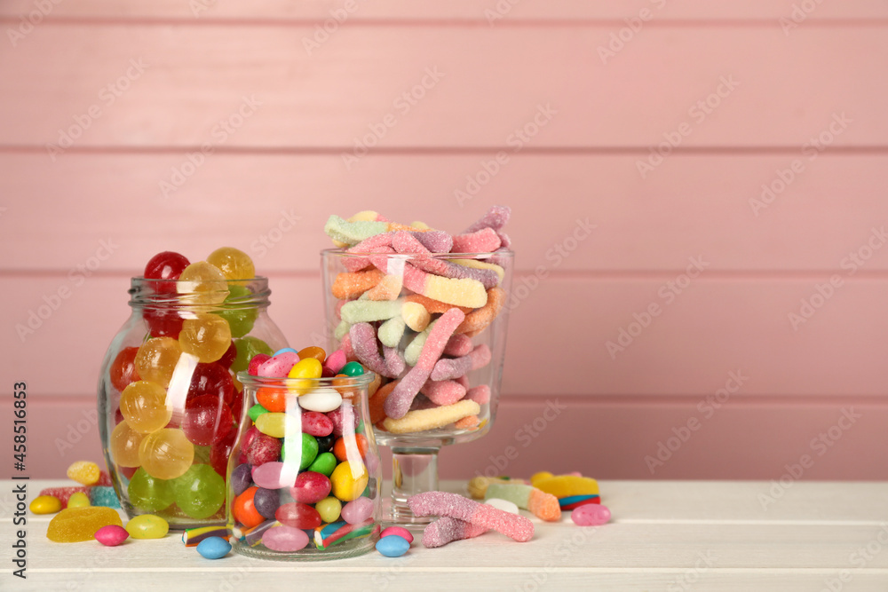 Fototapeta premium Jars with different delicious candies on white wooden table against pink background, space for text