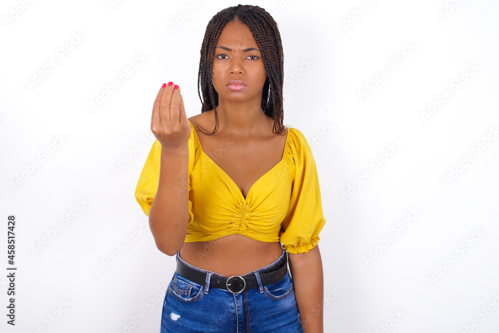 afro american woman with braids wearing sexy yellow t-shirt on white wall Doing Italian gesture with hand and fingers confident expression afro american woman with braids wearing sexy yellow t-shirt on white wall Doing Italian gesture with hand and fingers confident expression