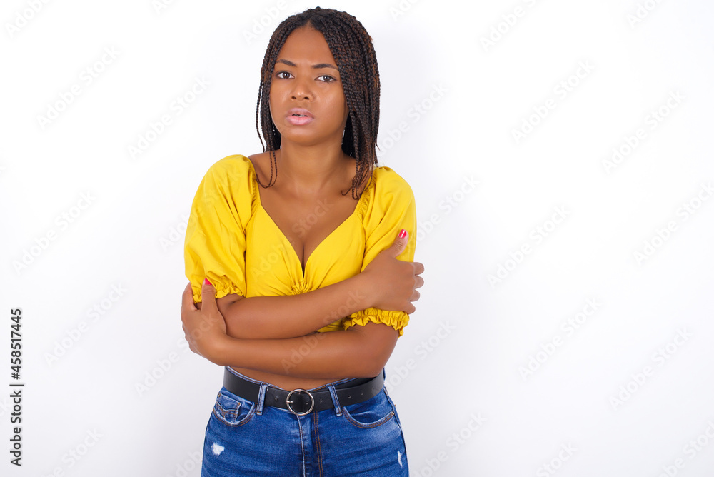 afro american woman with braids wearing sexy yellow t-shirt on white wall shaking and freezing for winter cold with sad and shock expression on face. afro american woman with braids wearing sexy yellow t-shirt on white wall shaking and freezing for winter cold with sad and shock expression on face.