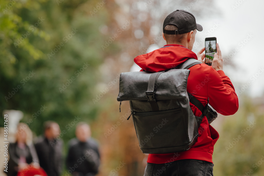 Back view man tourist with backpack photographing city on smartphone camera, autumn day Back view man tourist with backpack photographing city on smartphone camera, autumn day