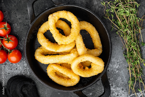 Fried squid rings breaded calamari appetizer on cast iron frying pan skillet, on black dark stone table background, top view flat lay