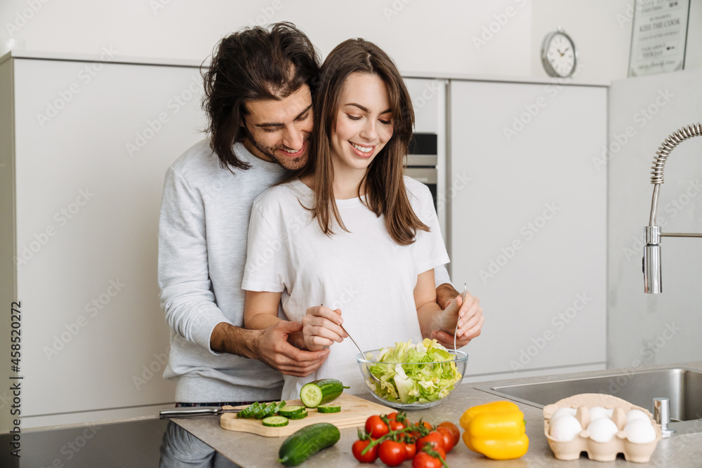 Young multiracial couple hugging while making salad together Young multiracial couple hugging while making salad together