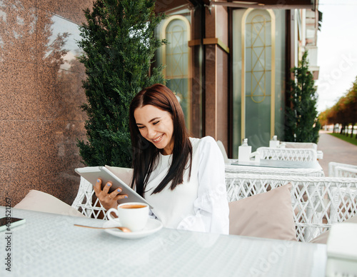 The girl sits in a cafe using technology. the girl looks at a teleon in a cafe at a table. photo