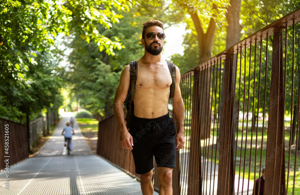 Athletic man with beard and naked torso walks in the park. He returns from the street workout.