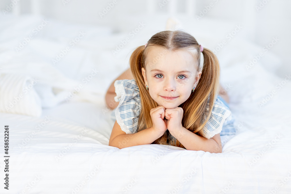 a girl child on the bed at home on a white cotton bed lies and smiles sweetly a girl child on the bed at home on a white cotton bed lies and smiles sweetly