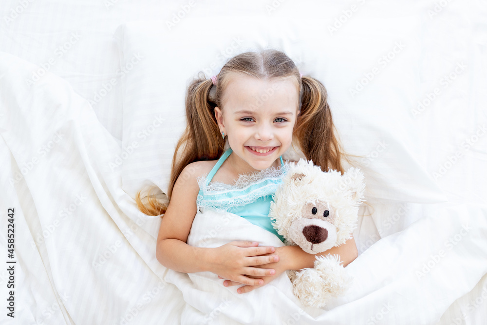 a baby girl is sleeping or woke up in the morning on the bed at home on a white cotton bed hugging a teddy bear toy in her hands and smiling sweetly a baby girl is sleeping or woke up in the morning on the bed at home on a white cotton bed hugging a teddy bear toy in her hands and smiling sweetly
