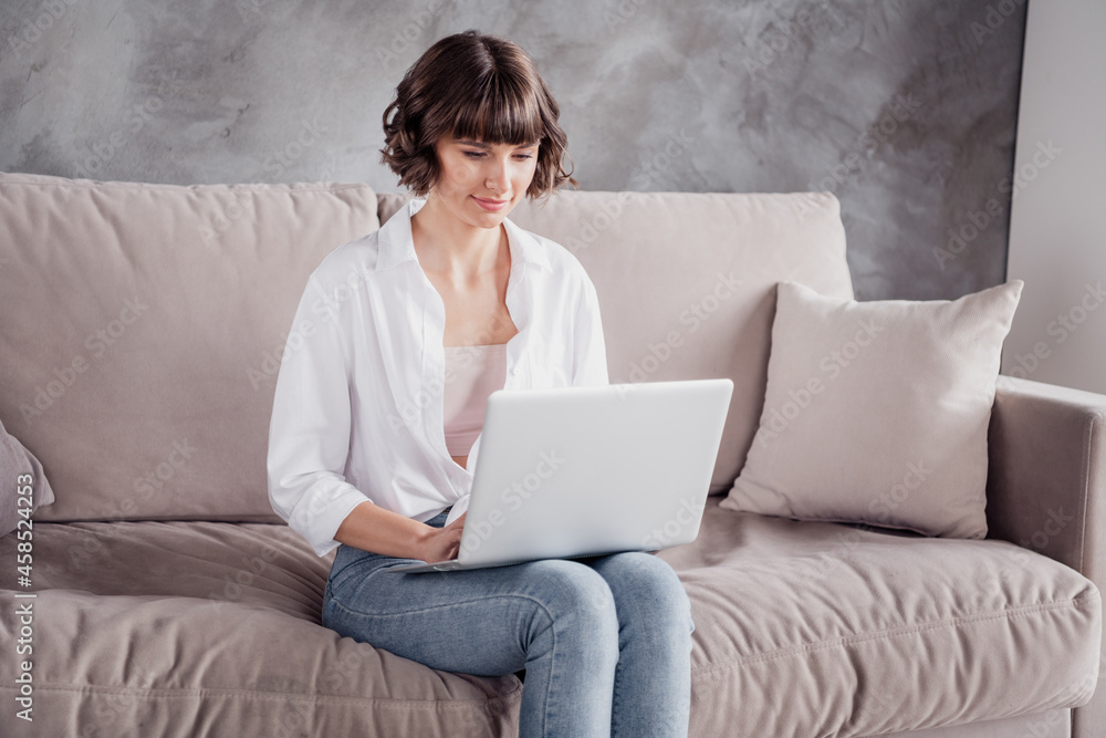 Naklejka premium Photo portrait woman wearing white shirt jeans sitting on sofa at home smiling using laptop
