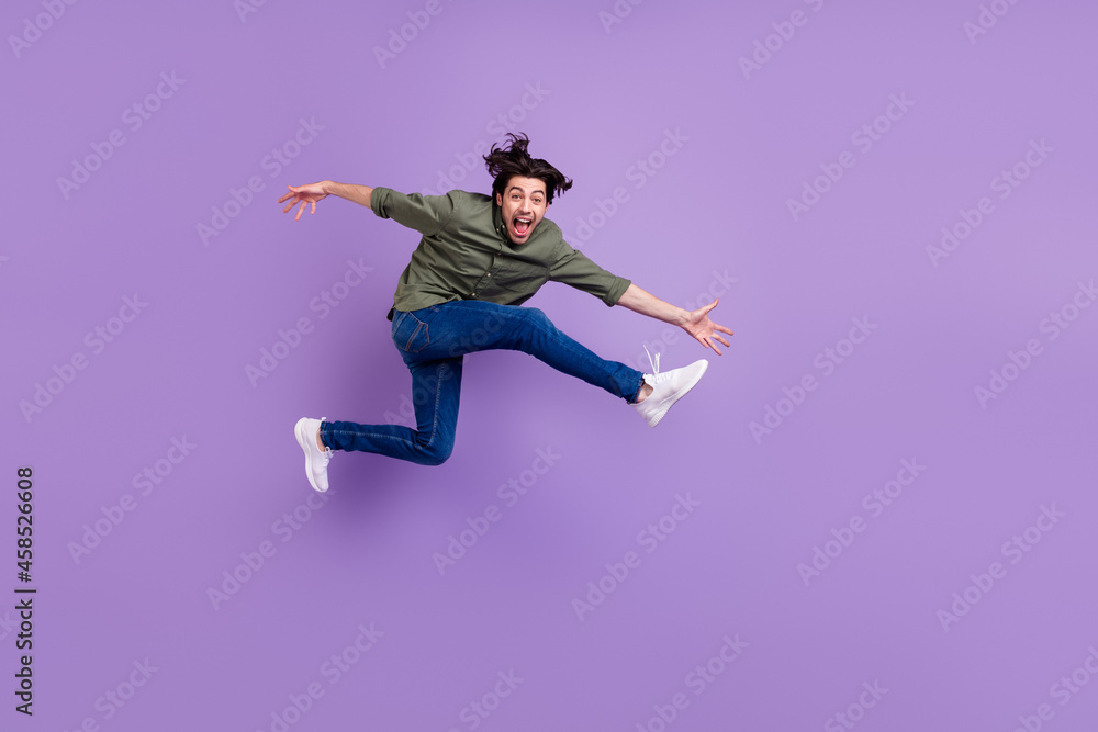 Full size photo of crazy positive happy young man jumper up run empty space cool isolated on purple color background Full size photo of crazy positive happy young man jumper up run empty space cool isolated on purple color background