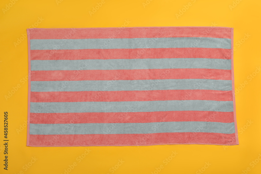 Striped beach towel on yellow background, top view