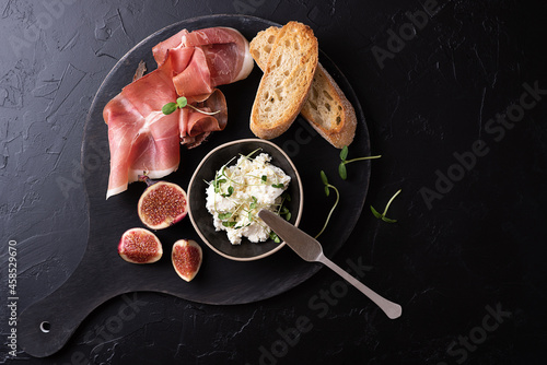 Dry cured ham with slices of bread on a black background, Italian appetizer prosciutto with fruit and cheese. photo