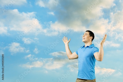 Young man rising on blue sky white clouds abstract background. Freedom feel good