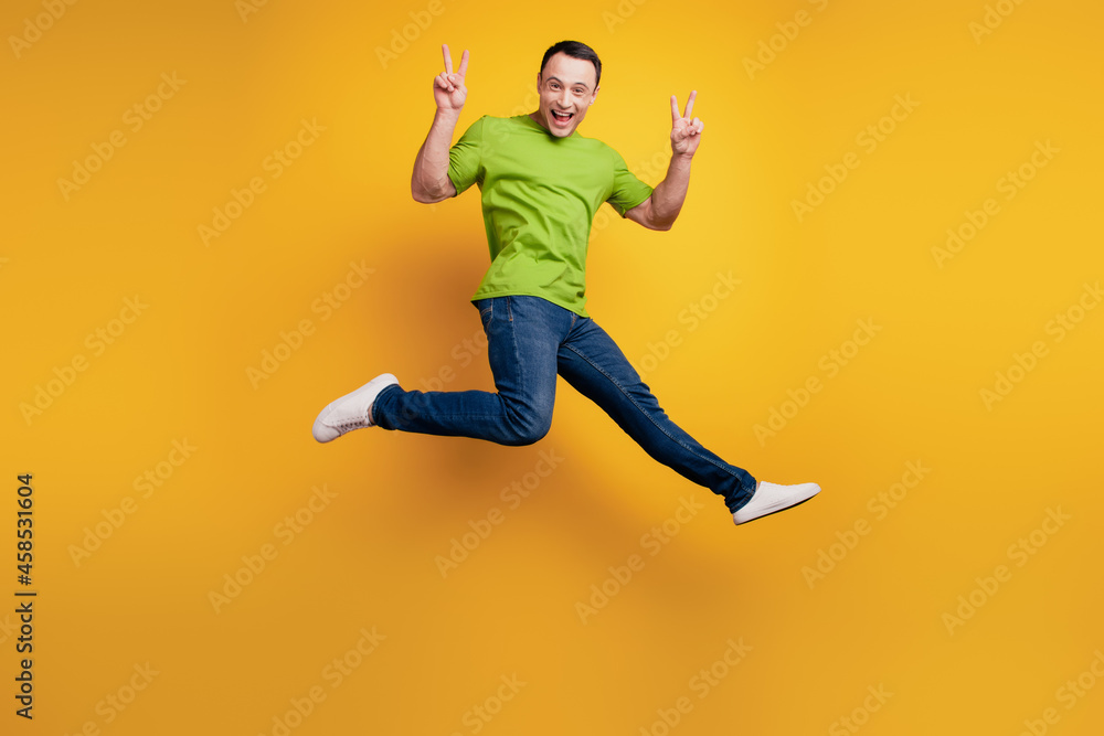 Portrait of funky excited energetic guy jump show v-sign on yellow wall