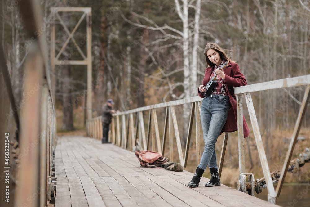 Young woman playing ukulele guitar in bridge in autumn forest