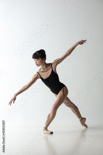 One young and graceful ballerina dancing isolated on light gray studio background. Art, motion, action, flexibility, inspiration concept.