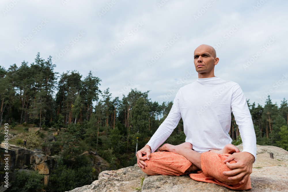 buddhist in sweatshirt looking away while meditating in lotus pose outdoors
