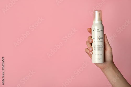 MYKOLAIV, UKRAINE - SEPTEMBER 09, 2021: Woman holding bottle of Kerastase hair care cosmetic product on pink background, closeup. Space for text photo