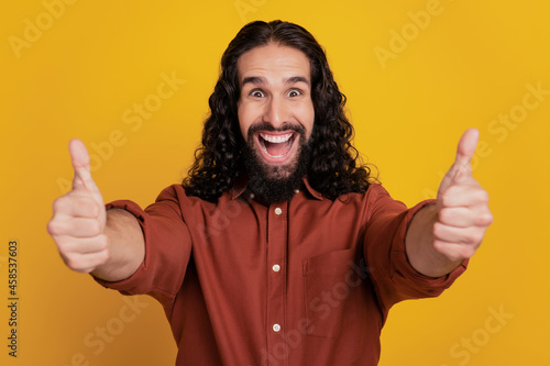 Portrait of excited funky positive guy raise hand show thumb up sign on yellow background