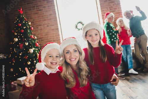 Photo portrait of happy mother smiling embracing son and daughter showing v-sign on xmas