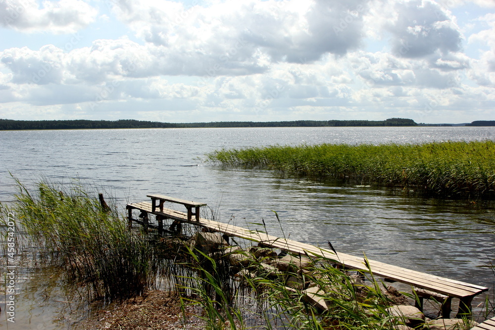 Lake with green ridges, sunny summer day with clouds in the sky, Lake Usma in Latvia. wooden footbridges in the lake 
