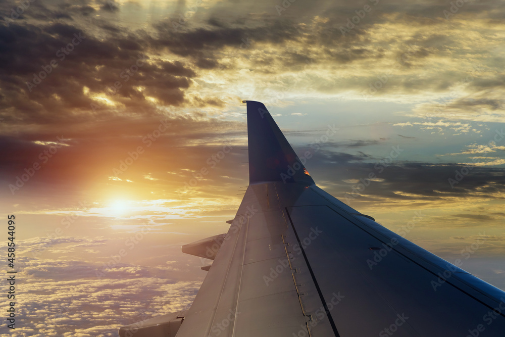 Wing of plane over dramatic white fluffy clouds on blue sky during sunset Wing of plane over dramatic white fluffy clouds on blue sky during sunset