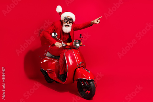 Photo of funky pretty motorcyclist dressed christmas costume eyewear pointing empty space hurrying isolated red color background