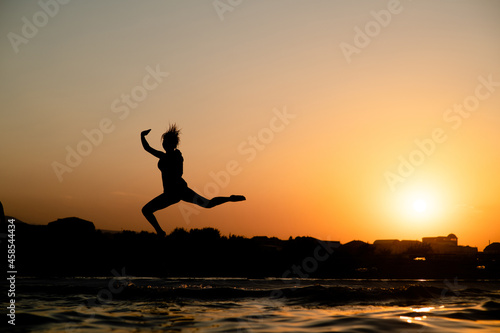 Happy girl having fun and jumps at sunset beach in sunlight. Summer vacation and healthy lifestyle concept. Empty space for text