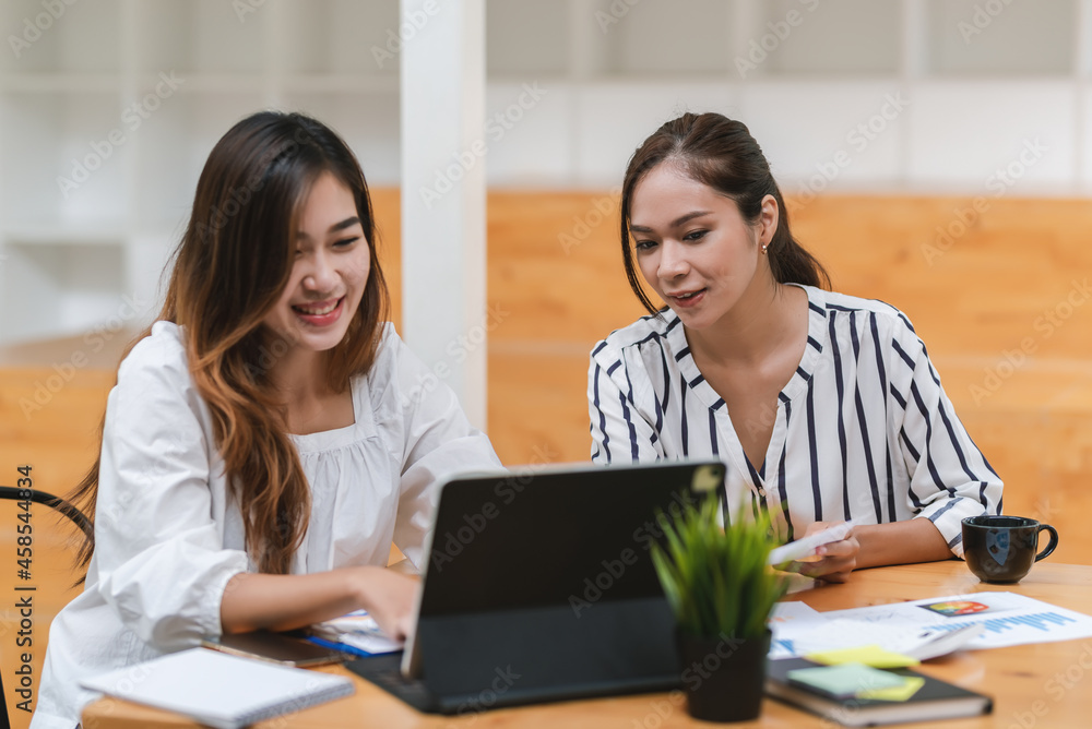 Team work of happy young Asian businesswoman analyze brainstorming together using a tablet the graph is placed on the office desk. Team work of happy young Asian businesswoman analyze brainstorming together using a tablet the graph is placed on the office desk.