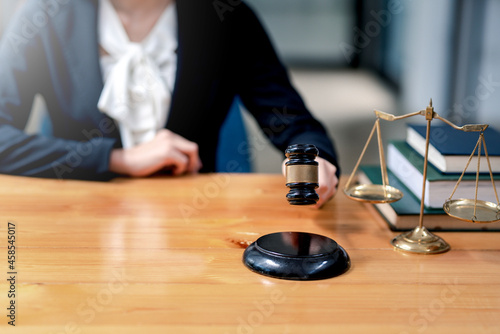 Close-up of businesswoman or lawyer woman hands knocking hammer judge scales and paper at office desk legal work.