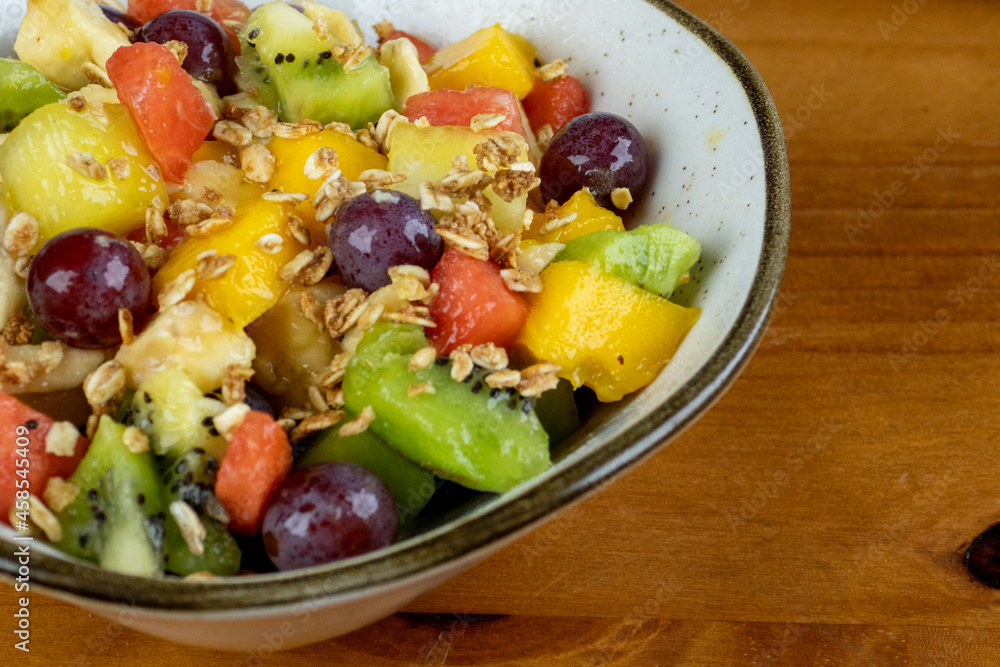delicious fresh tropical fruit salad served in white container for afternoon snack, photo taken sideways on wooden background with space for text beside