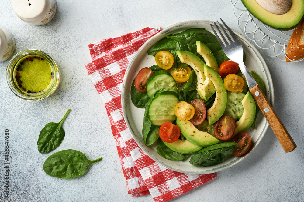 Avocado, red, yellow, black cherry tomato, spinach and cucumber fresh salad with spices pepper and olive oil in grey bowl on grey slate, stone or concrete background. Healthy food concept. Top view. Avocado, red, yellow, black cherry tomato, spinach and cucumber fresh salad with spices pepper and olive oil in grey bowl on grey slate, stone or concrete background. Healthy food concept. Top view.